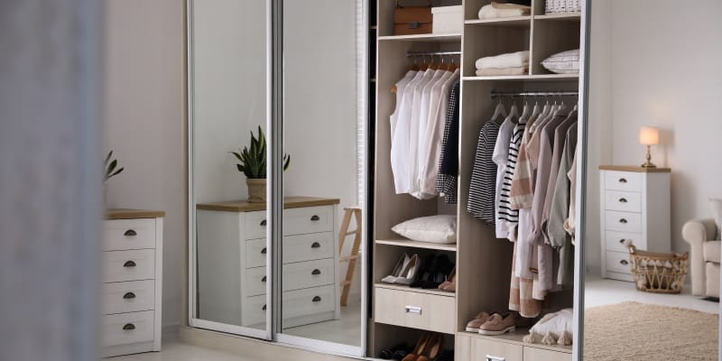 Wardrobe with full-length mirror fixed on its hinged doors in a small, tidy bedroom.